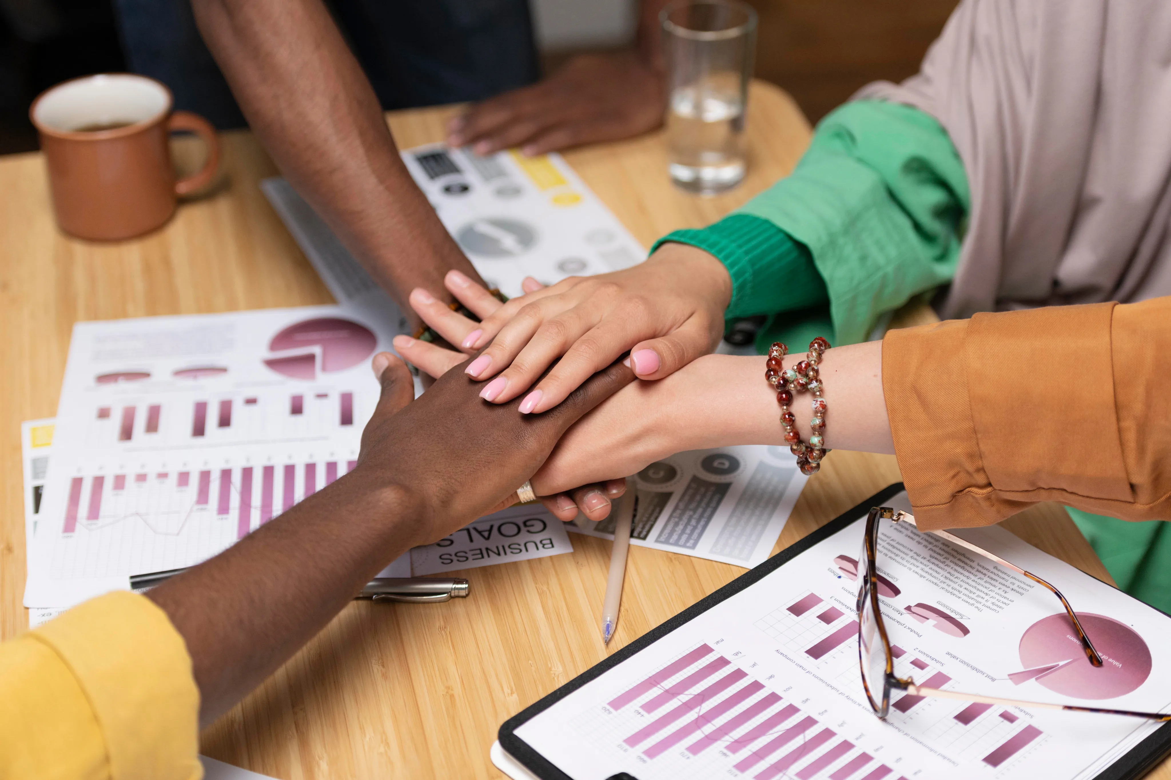 Team hands together over a desk with performance charts and collaboration